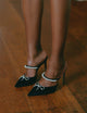 Zena Ziora luxury footwear capsule collection: Philippa pearl stiletto mule with crystal bow embellishment in black satin. Model standing up wearing both shoes; legs shown.